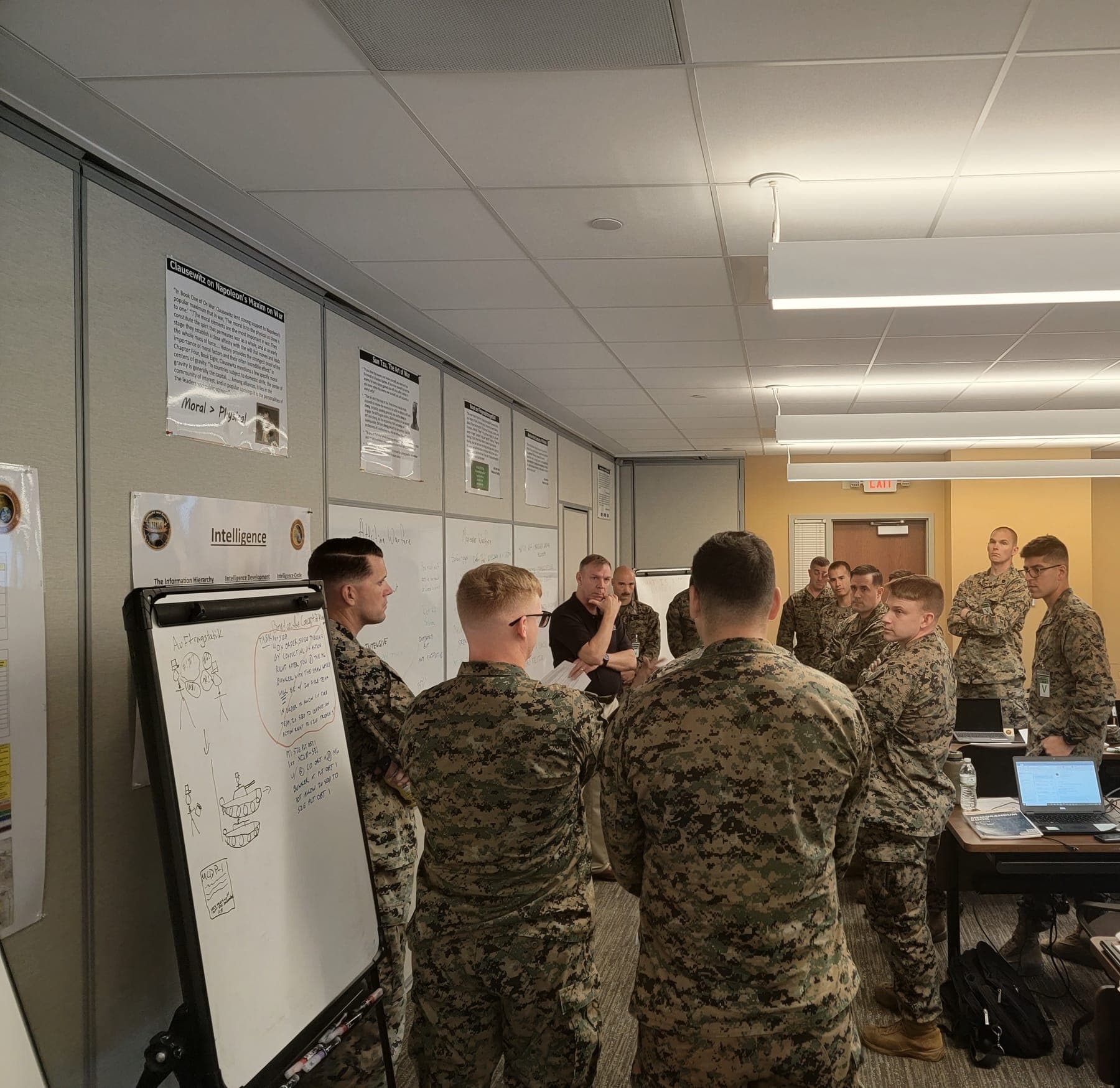 A group of Marines and instructors gathered around classroom whiteboards during a command and control training session